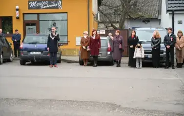 widzimy pana Burmistrza m&oacute;wiącego przez mikrofon oraz grupe os&oacute;b stojącą obok niego