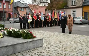 widzimy 2 panie stojące przed pomnikiem, w tle widoczne są sztandary