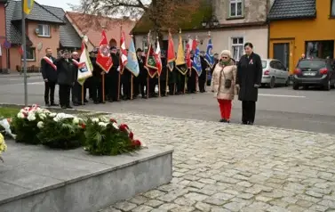 widzimy 2 panie stojące przed pomnikiem, w tle widoczne są sztandary