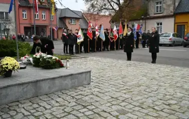 widzimy 2 panie stojące przed pomnikiem, w tle widoczne są sztandary