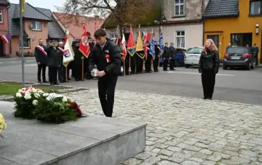 widzimy chłopaka kładącego na pomnik znicz, w tle widoczne są sztandary