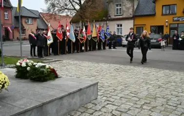 widzimy chłopaka i dziewczynę idącą w strone pomnika, w tle widoczne są sztandary