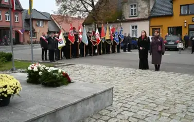 widzimy 2 panie stojące przed pomnikiem, w tle widoczne są sztandary