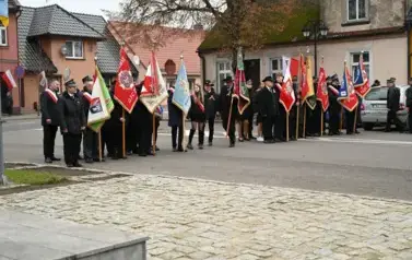 widzimy grupę os&oacute;b stojących ze sztandarami