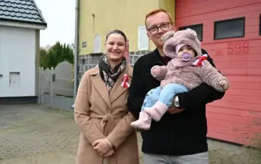 widzimy panią, pana oraz małe dziecko na tle budynku straży pożarnej