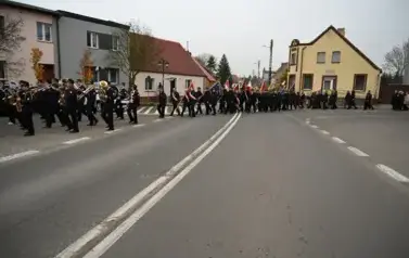 widzimy idącą po ulicy orkiestre, sztandary oraz grupe os&oacute;b