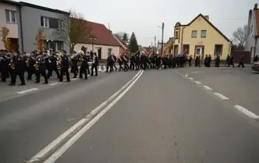widzimy idącą po ulicy orkiestre, sztandary oraz grupe os&oacute;b
