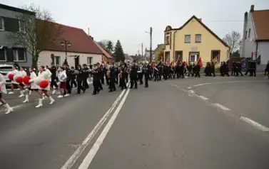 widzimy idące po ulicy dziewczyny z pomponami a za nimi idzie orkiestra oraz sztandary