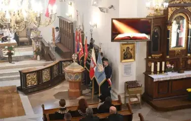 widzimy osoby stojące ze sztandarami oraz ołtarz 