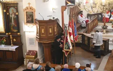 widzimy osoby stojące ze sztandarami oraz ołtarz 