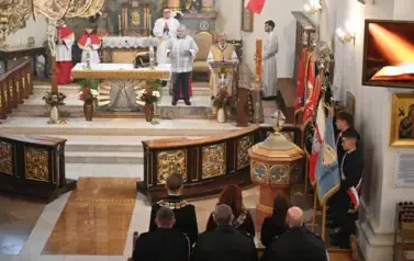 widzimy osoby stojące ze sztandarami oraz ołtarz 