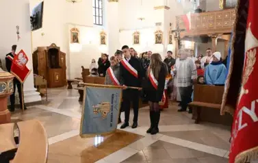 widzimy dużą ilość oso&oacute;b w kościele oraz idące osoby ze sztandarami