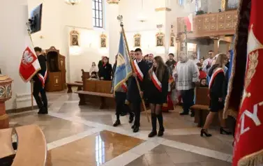 widzimy dużą ilość oso&oacute;b w kościele oraz idące osoby ze sztandarami