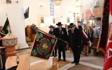 widzimy dużą ilość oso&oacute;b w kościele oraz idące osoby ze sztandarami