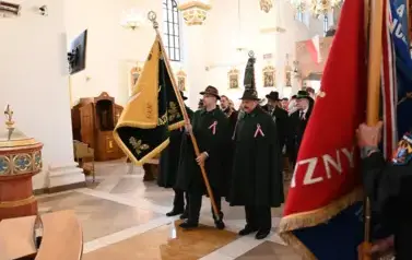 widzimy dużą ilość oso&oacute;b w kościele oraz idące osoby ze sztandarami