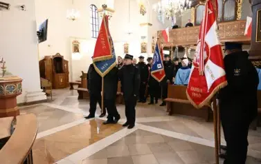 widzimy dużą ilość oso&oacute;b w kościele oraz idące osoby ze sztandarami