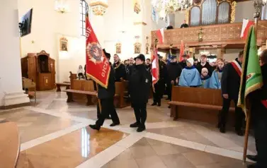 widzimy dużą ilość oso&oacute;b w kościele oraz idące osoby ze sztandarami