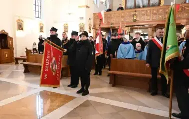 widzimy dużą ilość oso&oacute;b w kościele oraz idące osoby ze sztandarami