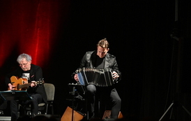 widzimy pana grającego na gitarze oraz drugiego pana grającego na akordeonie 