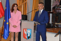 Na zdjęciu widać przemawiającego Radnego Gminy Mieścisko. Ubrany jest w granatowy garnitur. Przemawia przy m&oacute;wnicy z herbem Gminy Mieścisko.