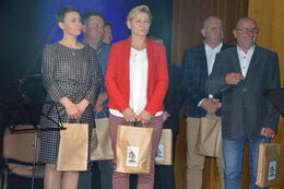 Na zdjęciu widać grupę ludzi na scenie. Są elegancko ubrani. W rękach trzymają nagrody.