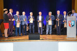 Na zdjęciu widać w&oacute;jta gminy, przewodniczącą rady oraz ośmiu eleganckich mężczyzn. Jedan z nich przemawia przy m&oacute;wnicy.