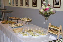 Zdjęcie przedstawia st&oacute;ł zastawiony przekąskami. Stoją ozdobne kielichy z kwiatami.