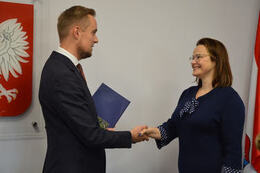 Na zdjęciu W&oacute;jt Gminy Mieścisko wręcza nagrodę pani dyrektor szkoły podstawowej. Kobieta ma ciemne, p&oacute;łdługie włosy. Ubrana jest w granatową sukienkę. Na twarzy ma okulary. Uśmiecha się.