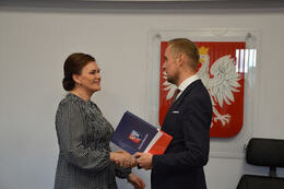 Na zdjęciu W&oacute;jt Gminy Mieścisko wręcza nagrodę nauczycielce w ciemnych, spiętych włosach. Uśmiechnięta kobieta ubrana jest w sukienkę w drobną, biało-czarną kratkę.