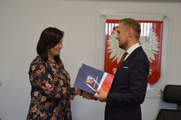 Na zdjęciu w&oacute;jt Gminy Mieścisko wręcza nagrodę nauczycielce ubranej w kwiecistą sukienkę. Ma ona ciemne, długie włosy.