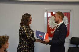 Na zdjęciu w&oacute;jt Gminy Mieścisko wręcza nagrodę nauczycielce w ciemnych, długich włosach, okularach. Ubrana jest w wzorzystą suknię.