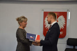 Na zdjęciu w&oacute;jt Gminy Mieścisko wręcza nagrodę nauczycielce w jasnych włosach, ubranej w sukienkę w drobną kratkę.