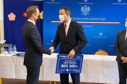 Na zdjęciu widać dw&oacute;ch mężczyzn w eleganckich garniturach. Jeden trzyma w ręce tabliczkę z kwotą jaką gmina otrzymała w ramach programu Polska Cyfrowa.