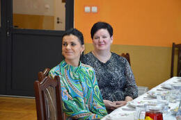 Na zdjęciu widac dwie kbiety siedzące przy stole. Pierwsza w ciemnych, spiętych włosach. Druga w kr&oacute;tkich, ciemnych włosach. Obie ubrane w kolorowe bluzki.