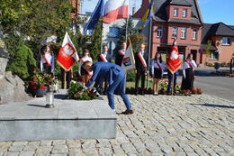 Na zdjęciu w&oacute;jt składa na pomniku wiązankę. W tle ustawione są sztandary.