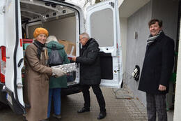 Zdjęcie przedstawia starszych ludzi wypakowujących prezenty z busa. 