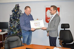 Zdjęcie przedstawia W&oacute;jta wręczajającego symboliczną premesę zwycięzcy projektu rejonowego. Jest to mężczyzna w granatowej koszuli i dżinsach.