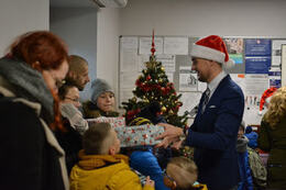 Na zdjęciu W&oacute;jt wręcza prezent dziecku. Obok stoją inne dzieci i dorośli.