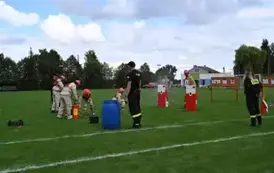 Młodzieżowa drużyna strażacka wykonuję zadanie konkurencyjne trafiając wężem z wodą do tarczy nalewowej