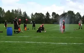 Młodzieżowa drużyna strażacka wykonuję zadanie konkurencyjne trafiając wężem z wodą do tarczy nalewowej