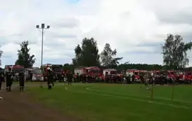 Strażacy stojący obok swoich woz&oacute;w strażackich