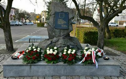 kamienny pomnik pamięci bohaterów z Gminy Mieścisko, na nim wiązanki kwiatów biało-czerwone  i płonące znicze