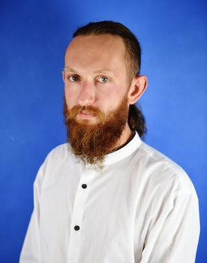 Zdjęcie przedstawia portret Radnego Rafała Borowiaka. Mężczyzna ma cioemne włosy spięte z tyłu, długa brązową brode z wąsem. Ubrany jest w białą koszulę z długim rękawem.